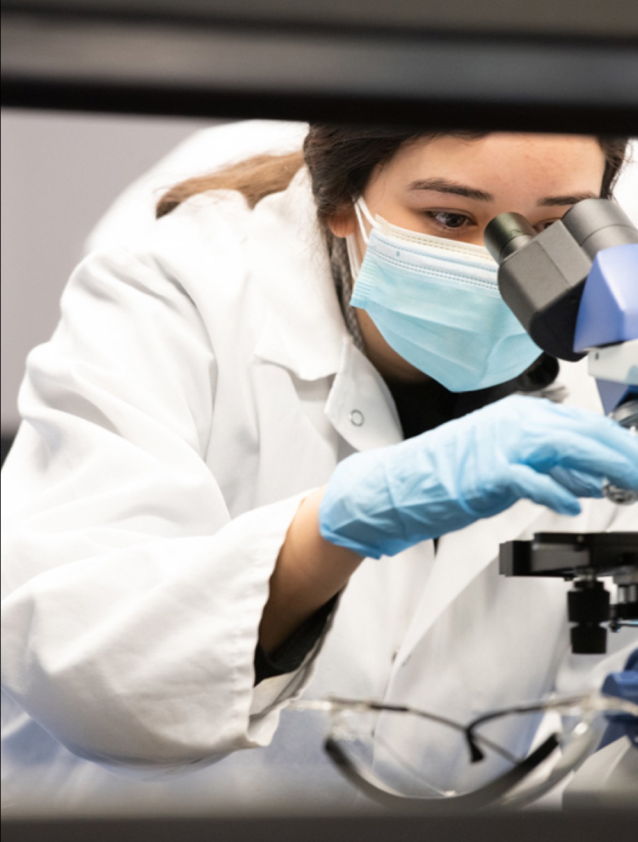 Student with a lab coat looking in a microscope.